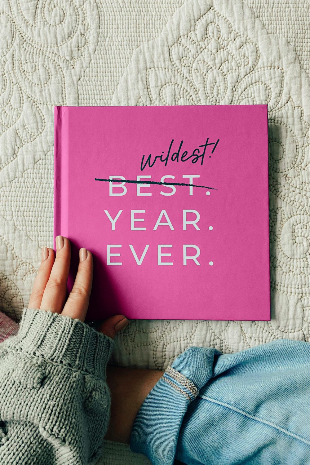 Woman in a khaki sweater, pink-white socks, and jeans holding a pink book titled Wildest Year Ever.
