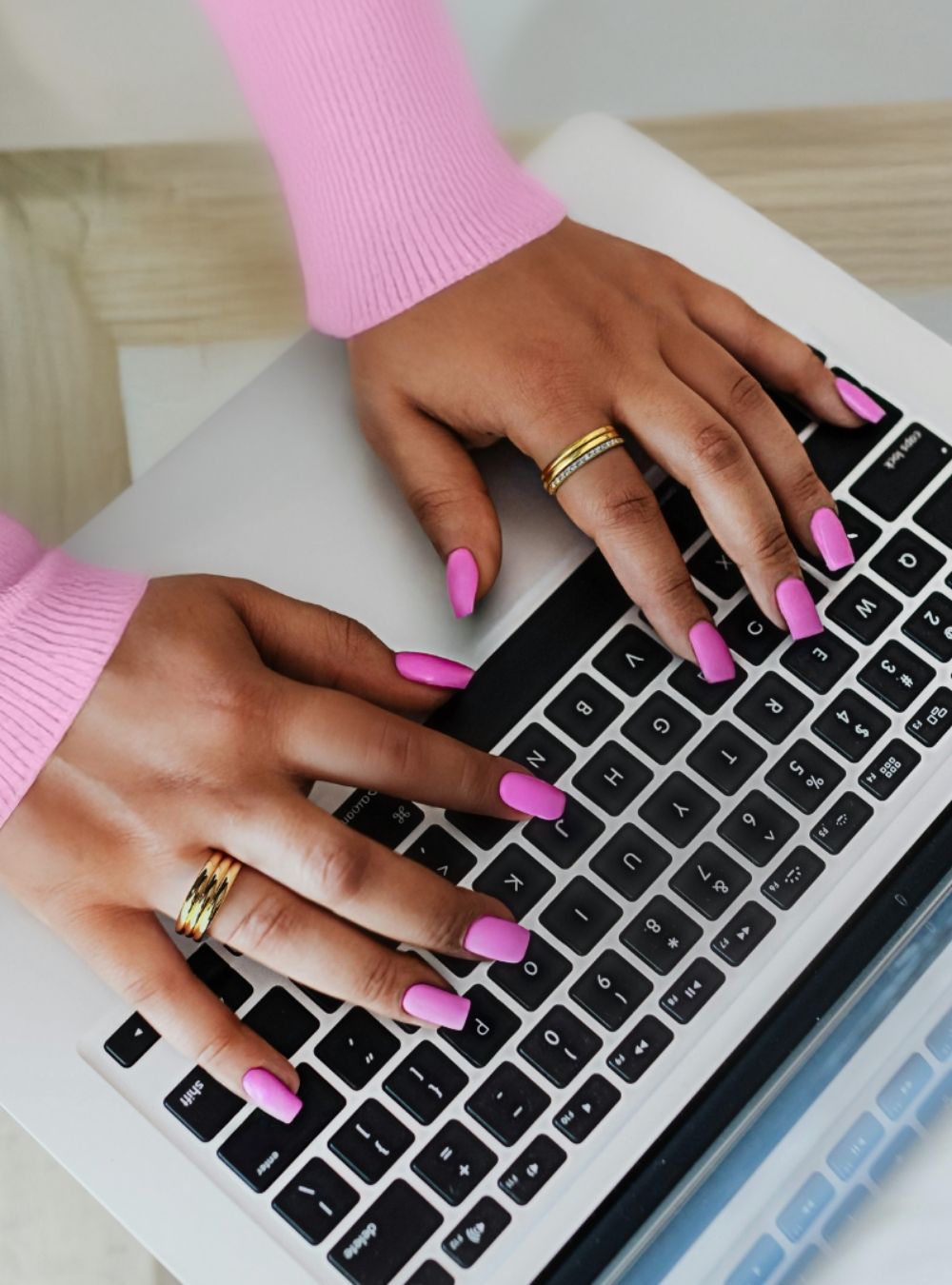 A woman wearing a pink sweater typing on a laptop, illustrating a solopreneur business blog workspace.