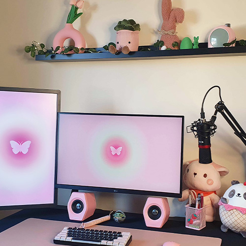 Gabi’s pink and black workspace with two monitors, pink donut vase, plush toys, and pink speakers.