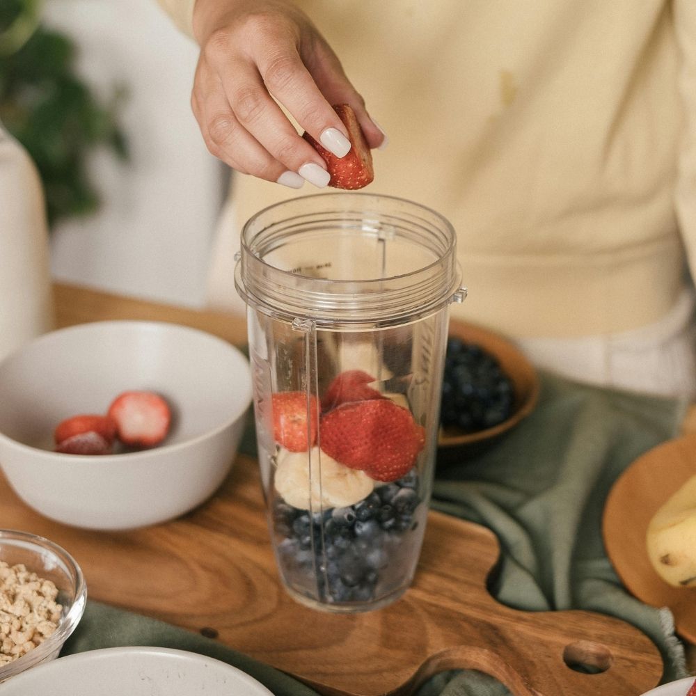 Person creating a healthy cocktail with berries and bananas.