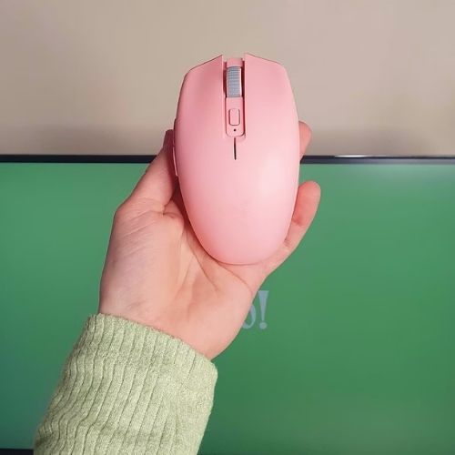 Hand displaying the pink Razer Orochi V2 wireless gaming mouse against a green screen background. This ergonomic and aesthetic tech essential is highly recommended for content creators for comfortable, long design and writing sessions.