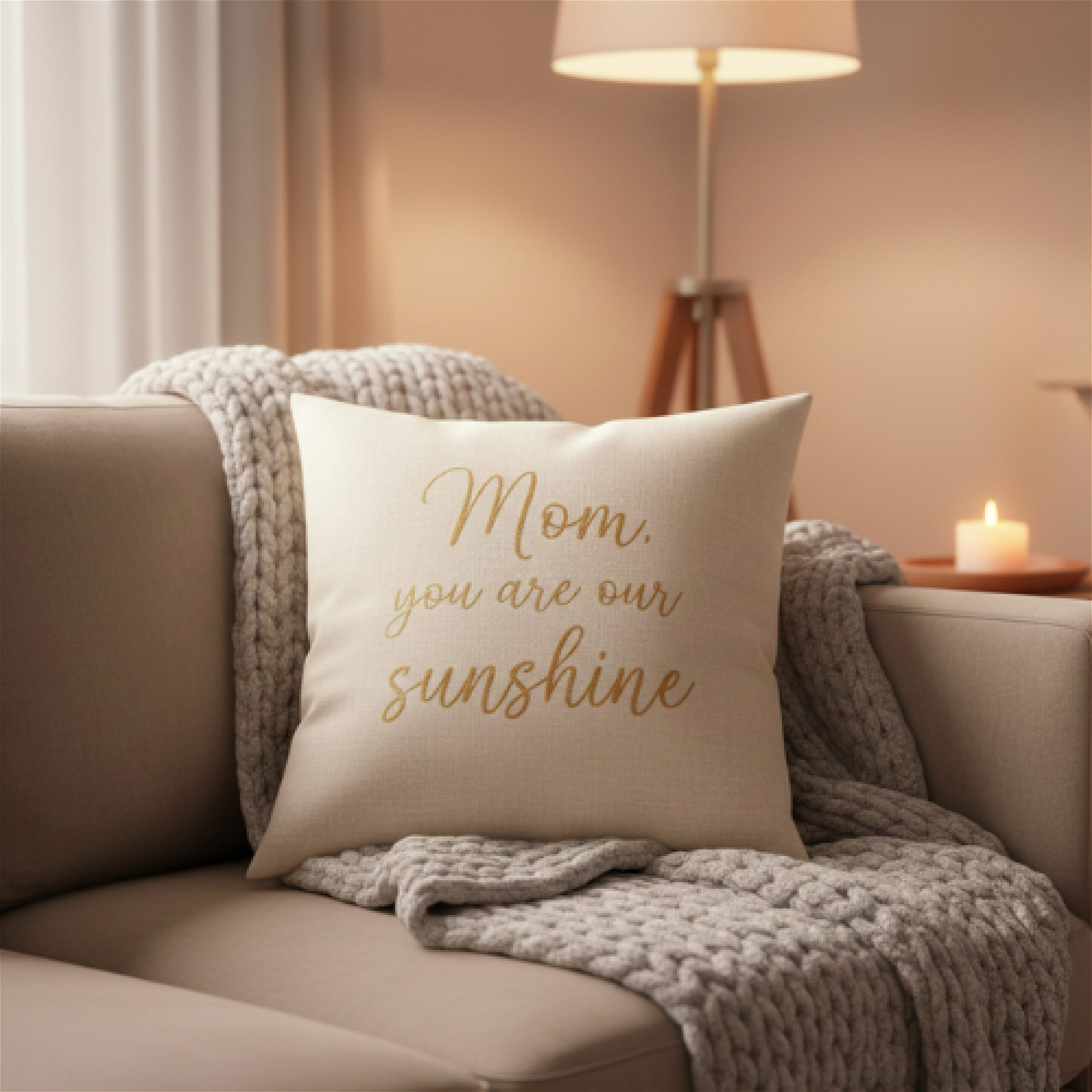Cozy living room scene with a decorative pillow on a sofa, reading "Mom, you are our sunshine." A knitted throw and a lit candle create a warm ambiance.