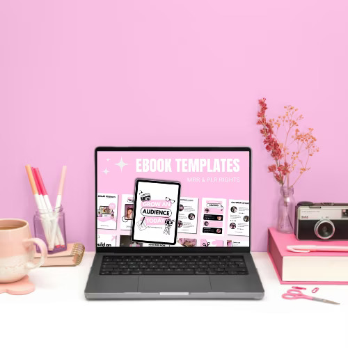 A laptop on a pink desk displays 'EBOOK TEMPLATES' on screen. Surrounding items include a pink mug, colorful pens, camera, and dried flowers, creating a creative and vibrant workspace.