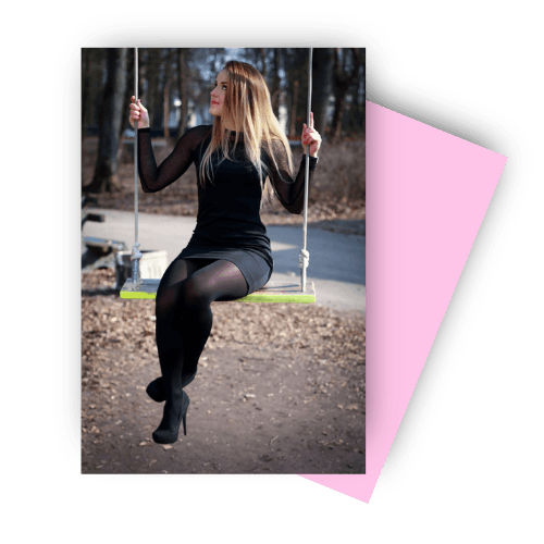 A woman in a black dress and heels sits on a swing looking to the side, with a park background of bare trees and fallen leaves, conveying a serene and contemplative mood.
