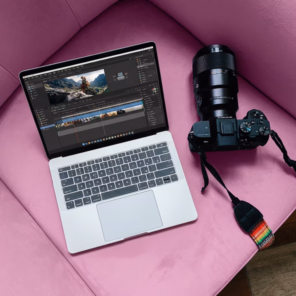 A laptop displays video editing software, next to a DSLR camera, resting on a plush pink chair. The scene conveys a sense of creativity and productivity.